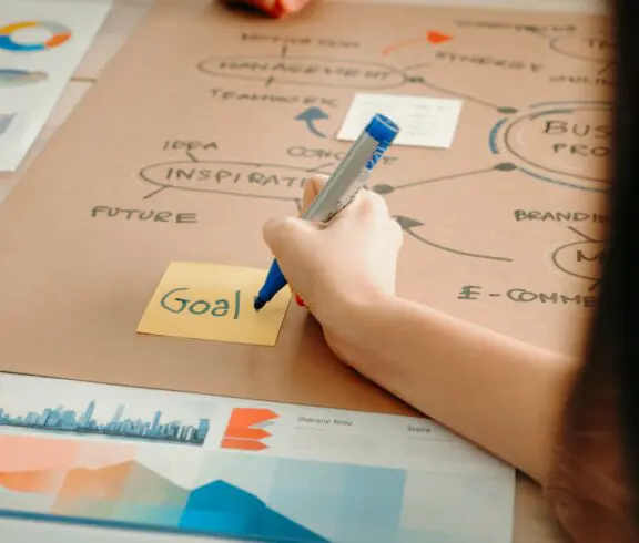 Hand writing "Goal" on sticky note.